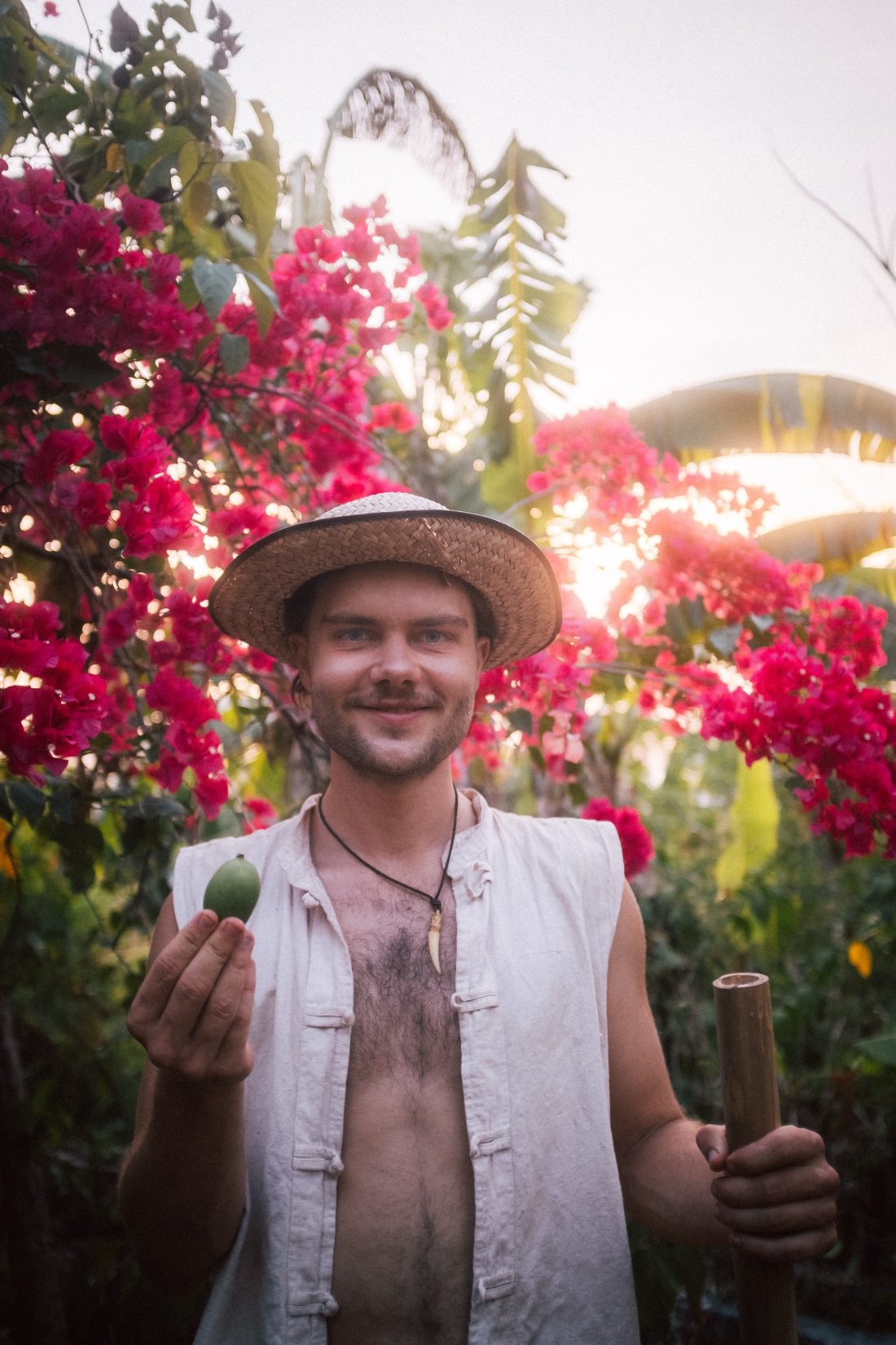 Aaron mit Strohhut zwischen blühenden Bougainvilleen, eine Frucht in der Hand